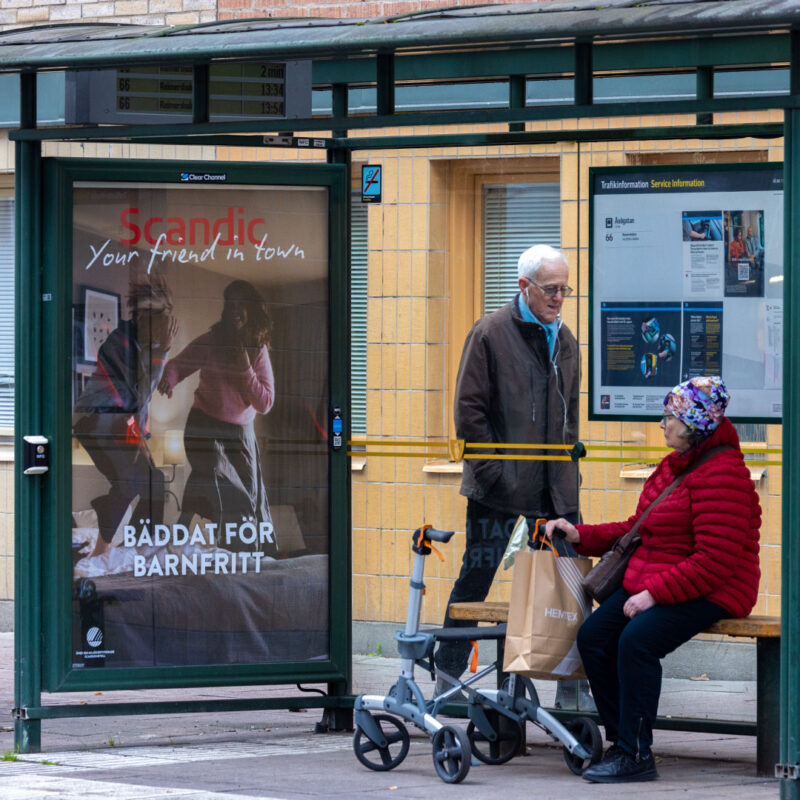 En pensionär med rullator som kollar på Scandic senaste kampanj på busshållplatsen