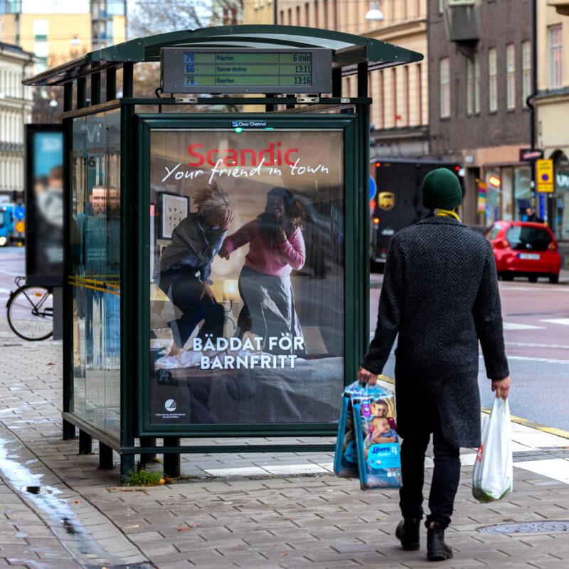 En man med matkassar som kollar på Scandic nya kampanj på busshållplatsen