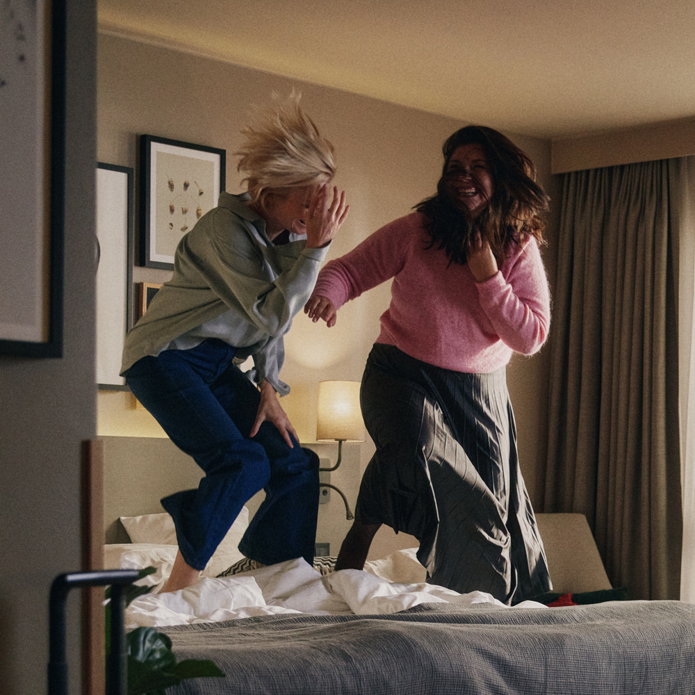 Två kvinnor som hoppar av glädje i en av Scandic Hotells härliga sängar